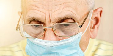 Gözlüklü yaşlı adam ve mavi tek kullanımlık yüz maskesi yakın plan.