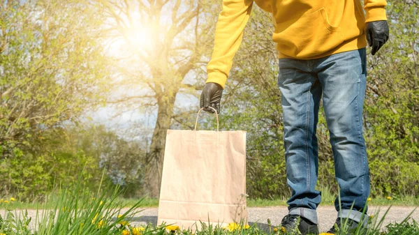 Mann in Kapuzenpulli und schwarzen Handschuhen legt Papiertüte auf Straße — Stockfoto