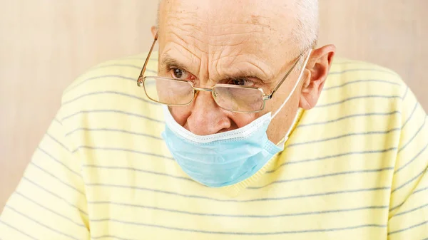 Hombre de edad avanzada en la máscara de la cara azul y gafas se ve a un lado primer plano —  Fotos de Stock