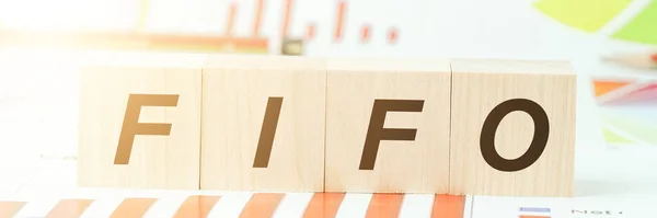 Písmena Fifo na dřevěných blocích na stole s různými grafy — Stock fotografie