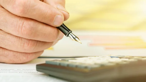 Pensioner hand writes with fountain pen by calculator close — Stock Photo, Image