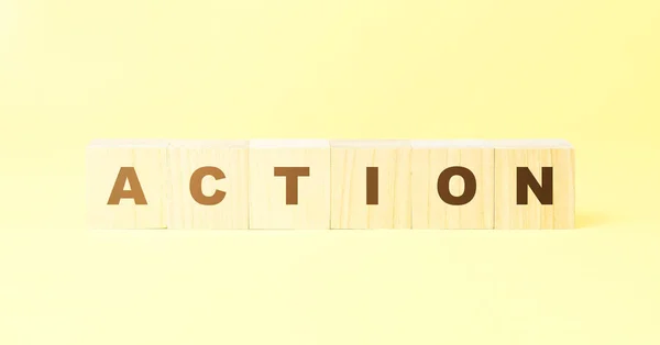 Woord actie gemaakt met houten blokjes op gele achtergrond — Stockfoto