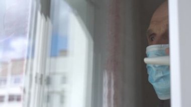Mavi maskeli yaşlı adam plastik pencereye yaklaşıyor.