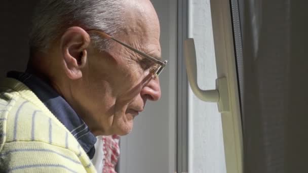 Homem sênior em óculos admira paisagem urbana em pé na janela — Vídeo de Stock