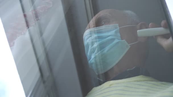 青い使い捨てマスクのシニア男はプラスチック窓に触れ — ストック動画