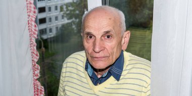 Sarı kazaklı yaşlı adam beyaz perdelerde duruyor.