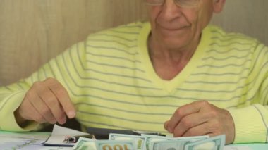 Gözlüklü yaşlı adam dolar toplayıp cebine koyar.
