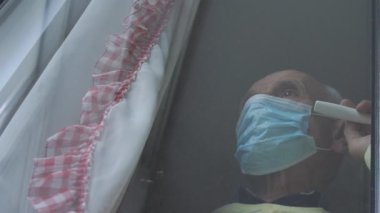 Steril maskeli depresif emekliler plastik pencereye dokunuyor