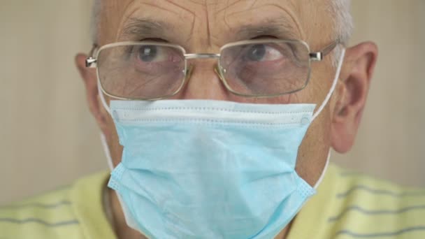 Homem idoso em azul máscara descartável e óculos olha ao redor — Vídeo de Stock