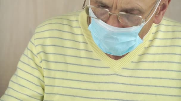 Senior man met bril en masker schrijft in pad aan tafel — Stockvideo