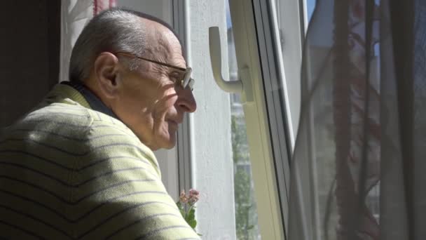 Старик в очках восхищается городским пейзажем, стоящим у окна — стоковое видео
