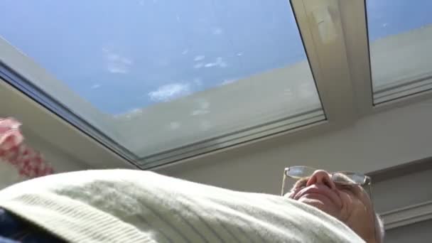 Hombre anciano abre cortinas y se extiende bajo la luz del sol — Vídeo de stock