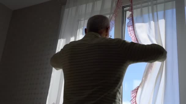 Pensionista en gafas abre cortinas y se extiende por la mañana — Vídeos de Stock