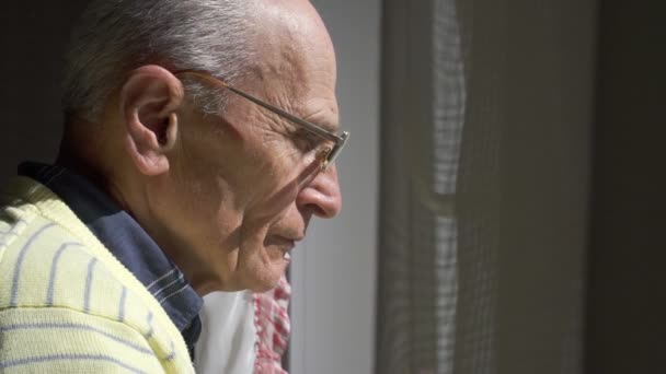 Concentré vieil homme dans des lunettes regarde par la fenêtre — Video