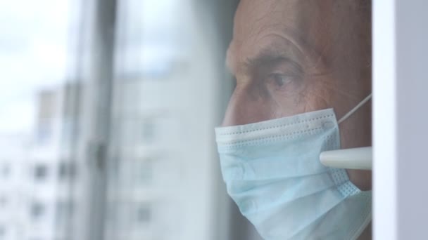 Old man in disposable mask waves hand at plastic window — Stock Video