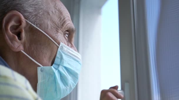 Homem velho em azul estéril máscara fica na janela de plástico branco — Vídeo de Stock