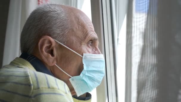 Oude man in blauw wegwerp masker sluit wit plastic venster — Stockvideo