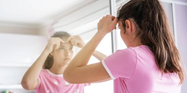 Uzun saçlı genç parmaklarıyla sivilceleri patlatır.