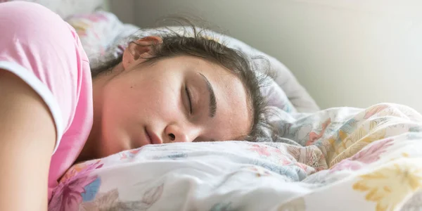 Tişörtlü kız büyük yatakta uyur, yastığa sarılır.