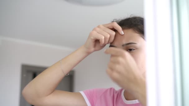 Triste jovem mulher aparece espinhas na testa com os dedos — Vídeo de Stock