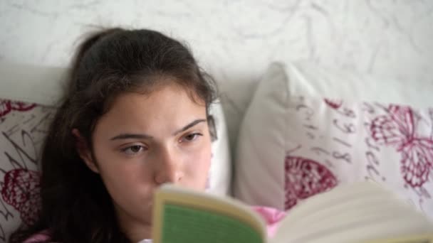 Adolescente con el pelo largo en cola de caballo se encuentra en la cama de lectura — Vídeos de Stock