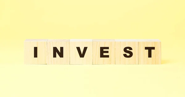 Słowo inwestować z czarnymi literami na drewnianych kostkach na żółty — Zdjęcie stockowe