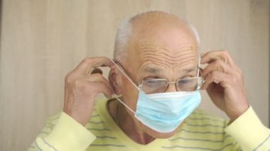Gözlüklü yaşlı adam evde mavi tek kullanımlık maske takıyor.