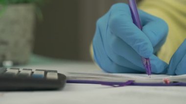 Mavi eldivenli eller deftere yazıp yakın plan hesaplar.