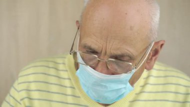 Steril maskeli yaşlı adam ve sarı kazak aşağı bakıyor.