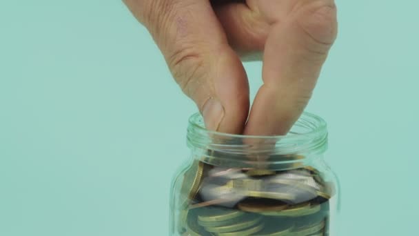 Gerimpelde vingers halen munten uit glazen pot closeup — Stockvideo
