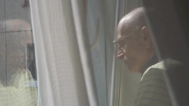 Размахивая занавеской, пенсионер стоит у белого окна — стоковое видео