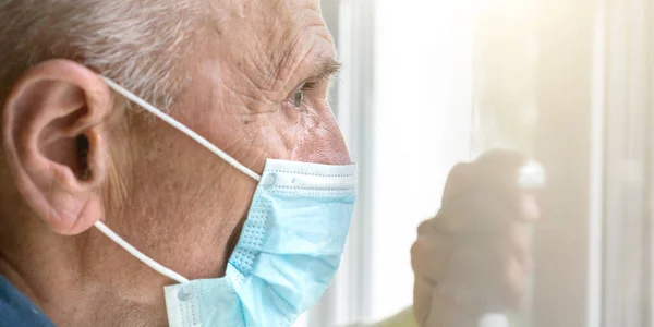 wrinkled man in mask looks straight with depression at home