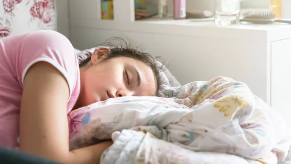 Młoda kobieta w t-shirt śpi na dużym łóżku i przytula koc — Zdjęcie stockowe