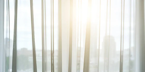 Gün ışığı şeffaf perdelerin arasından odaya doğru parlıyor.