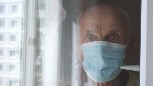 Spiegelbild eines alten Mannes mit blauer Maske, der am Fenster steht — Stockvideo