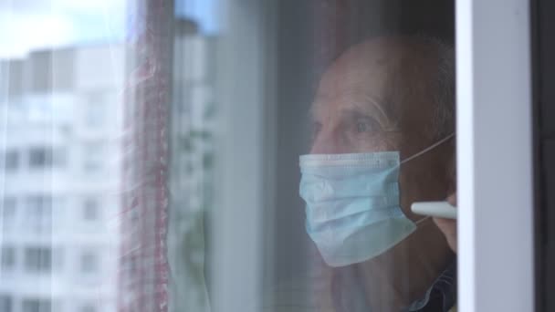 Rentner in Maske blickt durch Fensterscheibe auf die Straße — Stockvideo