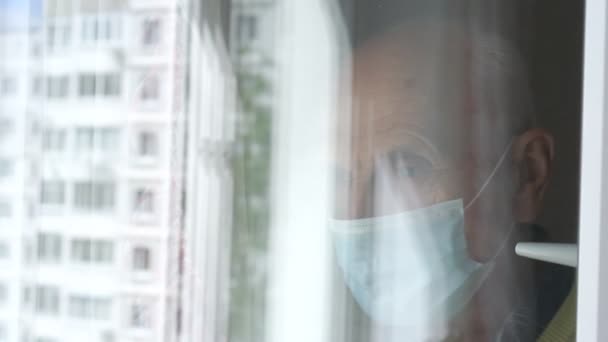 Отражение грустного старика в маске, машущего рукой в окно — стоковое видео