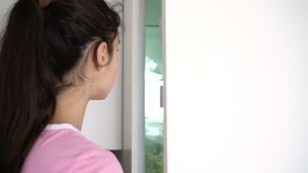Adolescente com cabelos longos em rabo de cavalo abre grande frigorífico branco — Vídeo de Stock