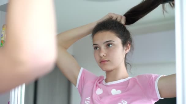 Teenager girl brushes ponytail reflecting in mirror closeup — Stock Video