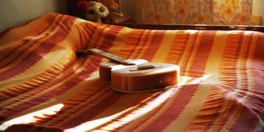 Kahverengi ahşap gitar çizgili battaniyeyle kaplı yatakta yatıyor.