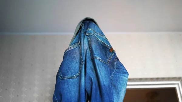 Blue denim jeans hang on door edge against white wall — Stock Photo, Image