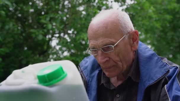 Senior man in bril leest het houden van grote plastic fles — Stockvideo