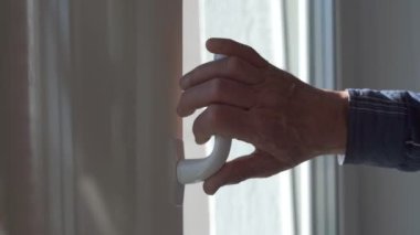 Yaşlı adam beyaz plastik sapıyla pencereyi kapatıyor.