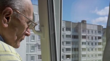 Gözlüklü yaşlı adam pencereden sokağa bakıyor.