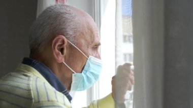 Mavi steril yüz maskeli emekli beyaz pencerenin yanında duruyor.