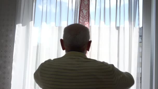 Pensionären öppnar gardiner går bort mot byggnaden utanför — Stockvideo
