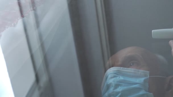 Schmerzgeplagter Mann mit blauer Maske lehnt an Plastikfensterscheibe — Stockvideo