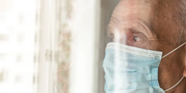 Mavi tek kullanımlık yüz maskeli emekli pencerenin dışına bakıyor