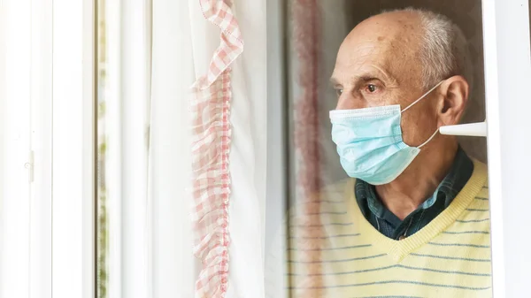 depressed pensioner in blue mask looks through window