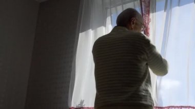 Gözlüklü yaşlı adam perdeleri kapatır ve odaya girer.